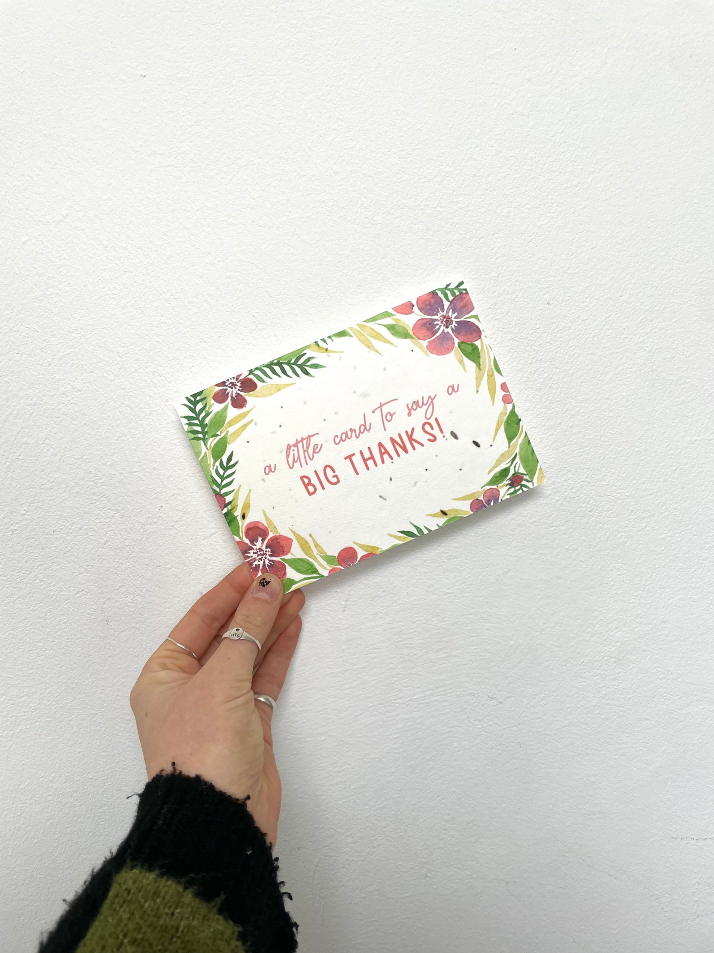 A hand holding a plantable seed card with a floral design and the text 'a little card to say a big thank!' along with a recycled Kraft envelope.