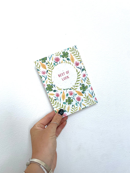 Hand holding a floral card with 'Best of Luck' text on a white background