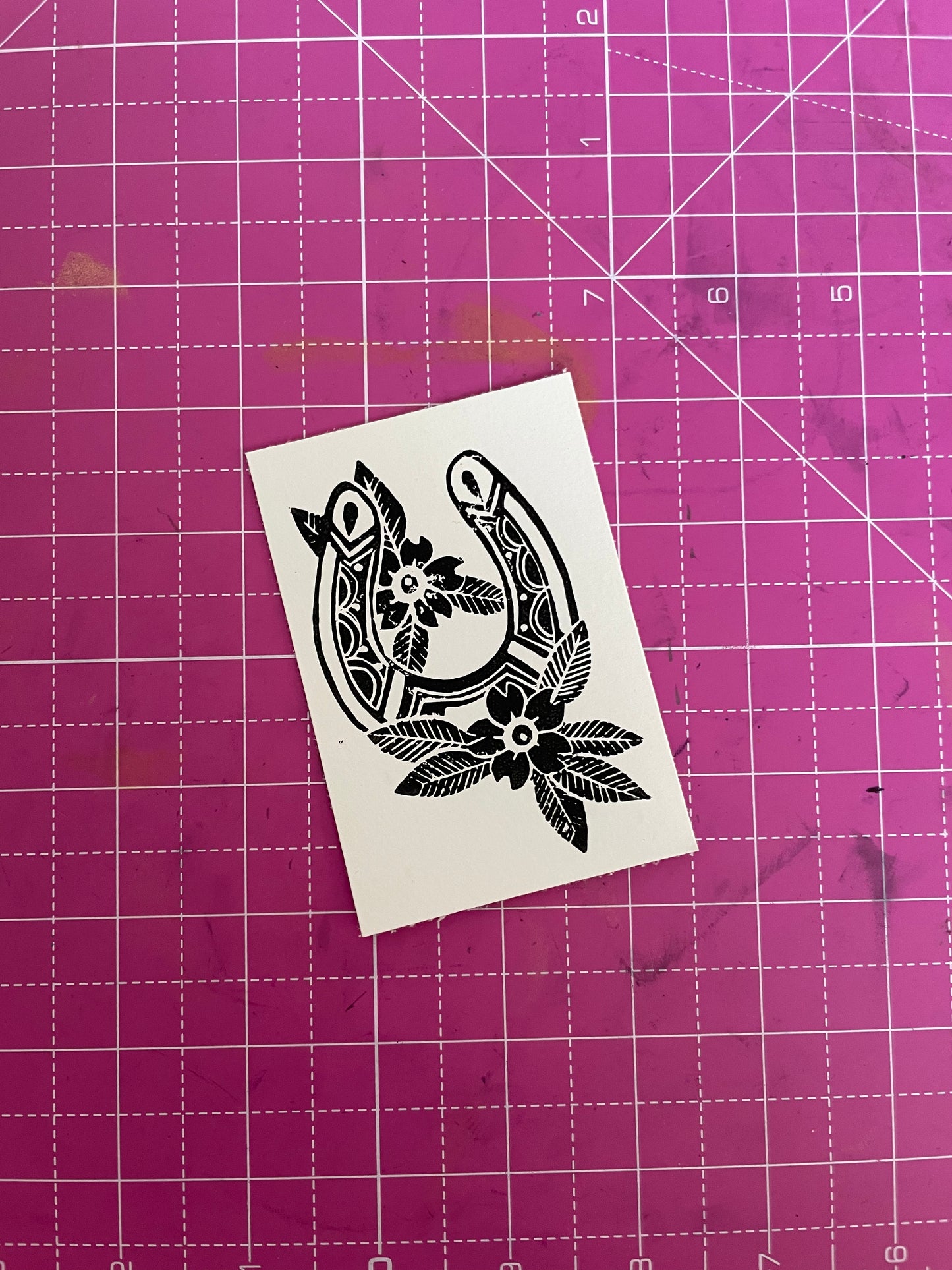 A lino print of a lucky cowboy horseshoe with flowers in black and white