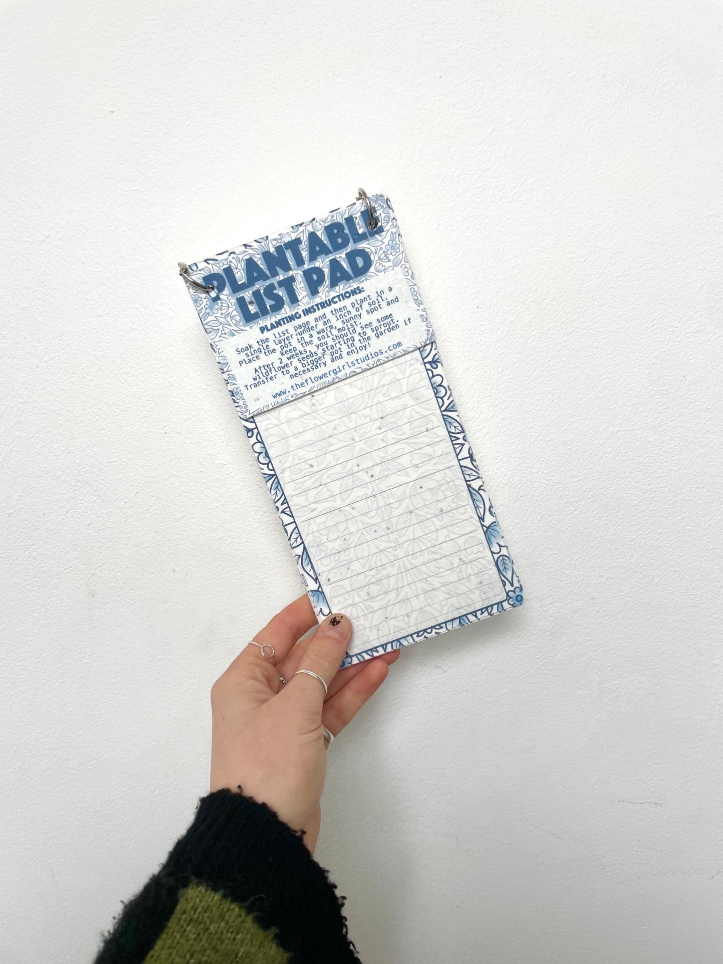 A hand holding a plantable list pad with blue floral pattern.